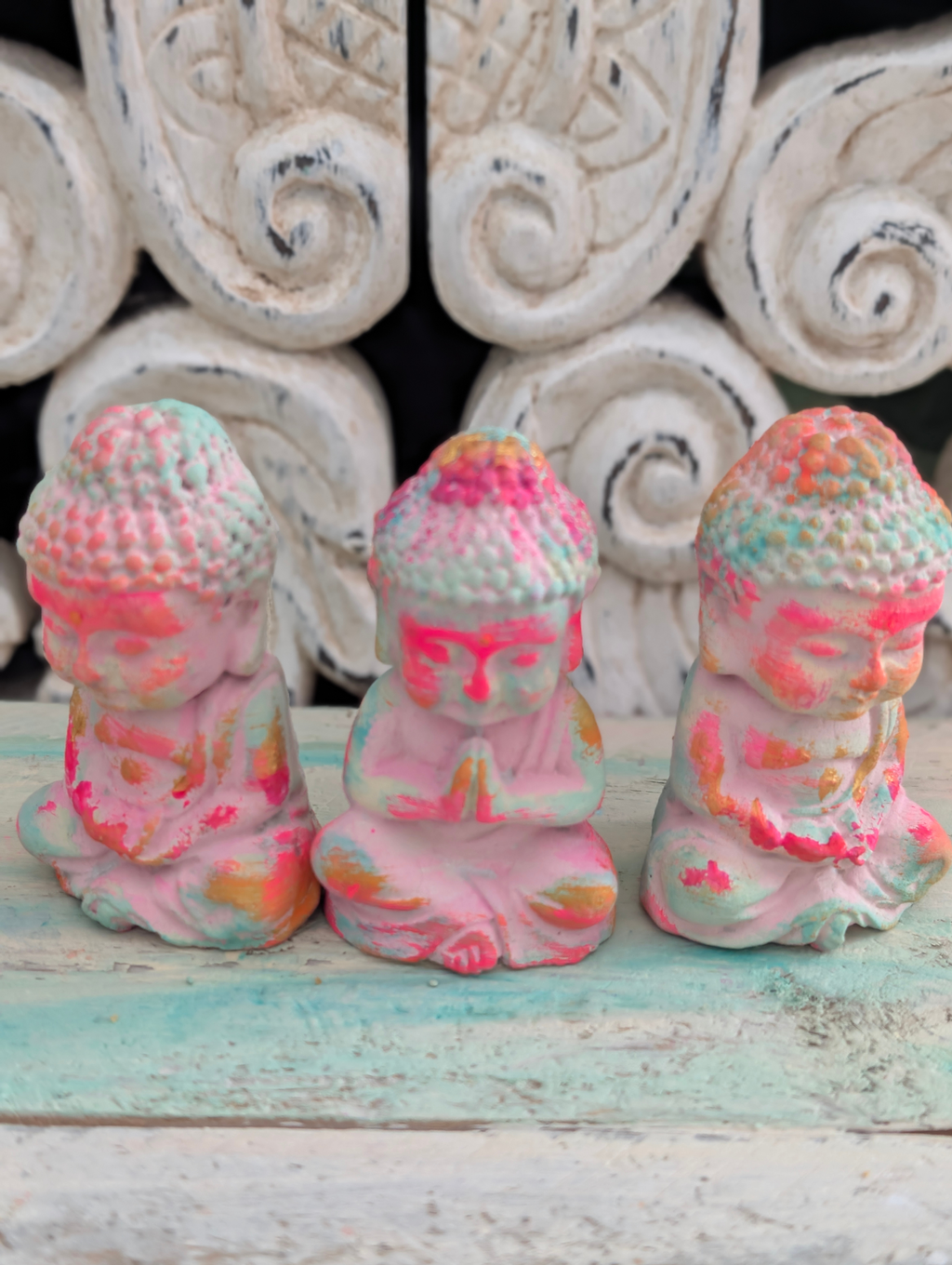 ANILUAP Buddha Trio in Neon-Pink und Mint vor weißem Ornament-Hintergrund – handgefertigte Steinfiguren für den Altar